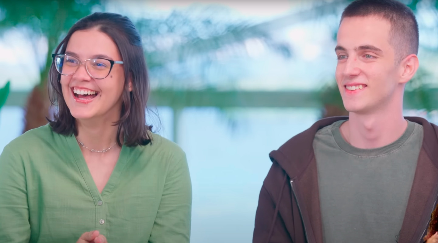 O apresentador Primak sorrindo em um ambiente iluminado, com plantas ao fundo.