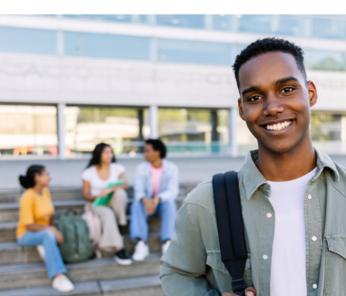 Estudante negro de mochila sorrindo em primeiro plano com estudantes atrás na escada conversando