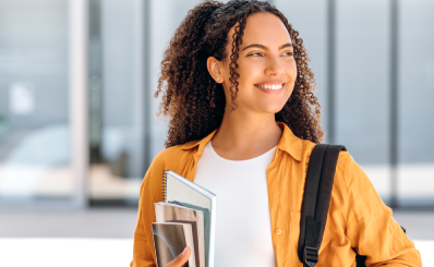 Estudante sorrindo e olhando para o lado segurando livros e apostilas.