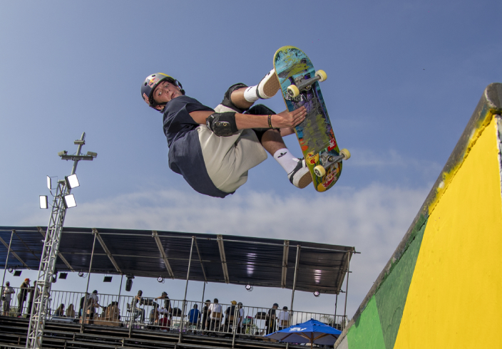 Atleta fazendo manobra em skate no ar, em uma pista.