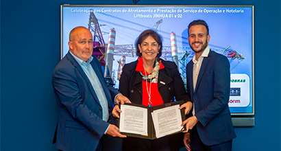 A diretora de Exploração e Produção da Petrobras, Sylvia Anjos, o CEO da OOS International, Leon Overdulve, e o vice-presidente da Camorim, Eduardo Adami seguram contrato assinado em cerimônia da Petrobras, com plataforma marítima ao fundo.