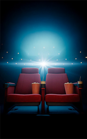 Duas poltronas de cinema com baldes de pipoca e bebidas, em frente a uma tela iluminada.