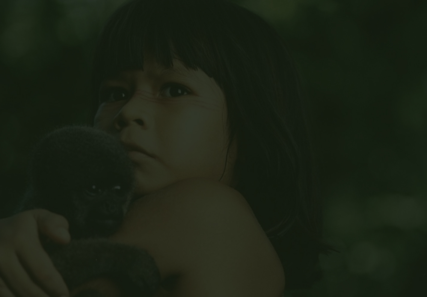 Close-up da personagem Tainá, uma menina indígena com pinturas faciais vermelhas, segurando um pequeno macaco no colo em meio à floresta.