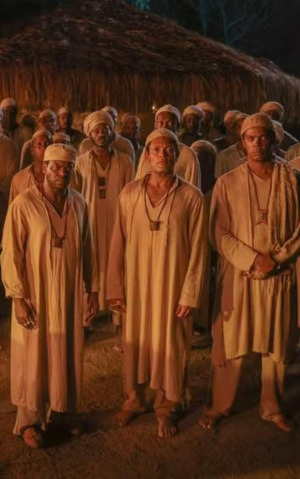Grupo de homens negros em trajes tradicionais reunidos à noite, em cena histórica ambientada em comunidade afro-brasileira.