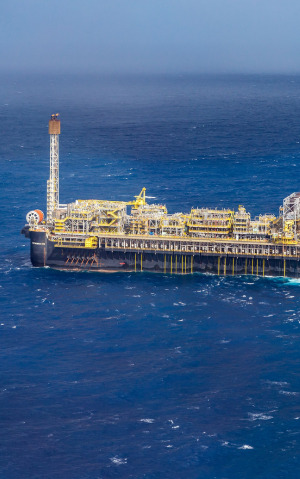 Vista aérea da plataforma FPSO P-66 operando em mar aberto, com seu casco escuro e complexa estrutura de processamento amarela sobre o convés.
