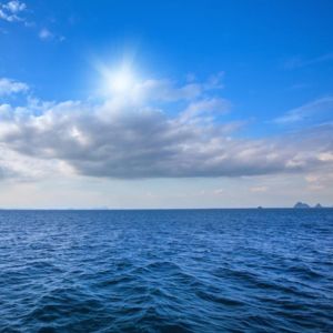 Vista panorâmica de um mar azul profundo sob um céu claro com sol brilhante e nuvens esparsas.