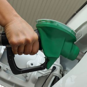 Close-up de uma mão segurando um bico de abastecimento verde inserido no tanque de um veículo branco.