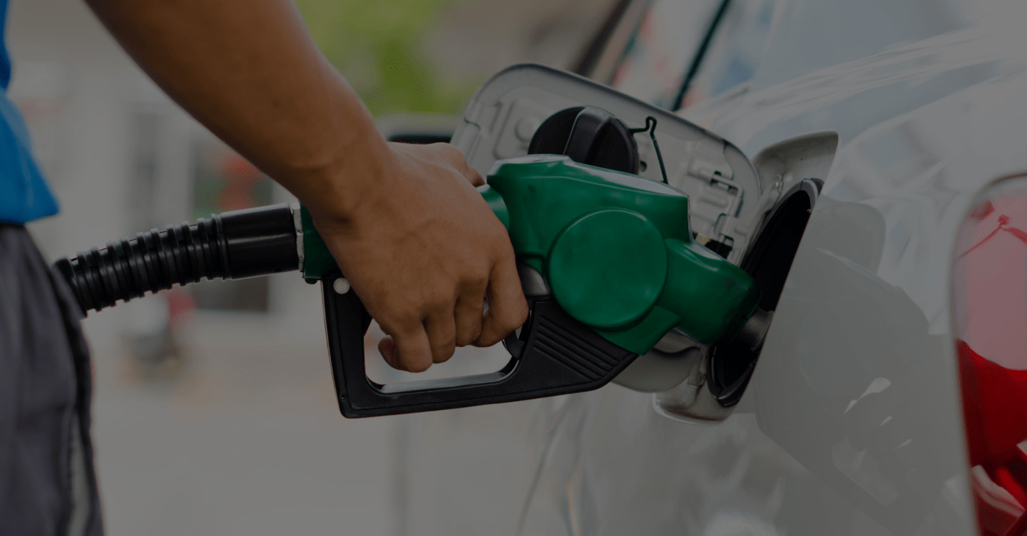 Mão abastecendo um carro com bico de combustível verde em posto de gasolina.