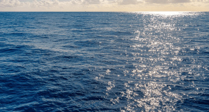 Superfície do oceano com reflexo do sol sobre o mar azul.