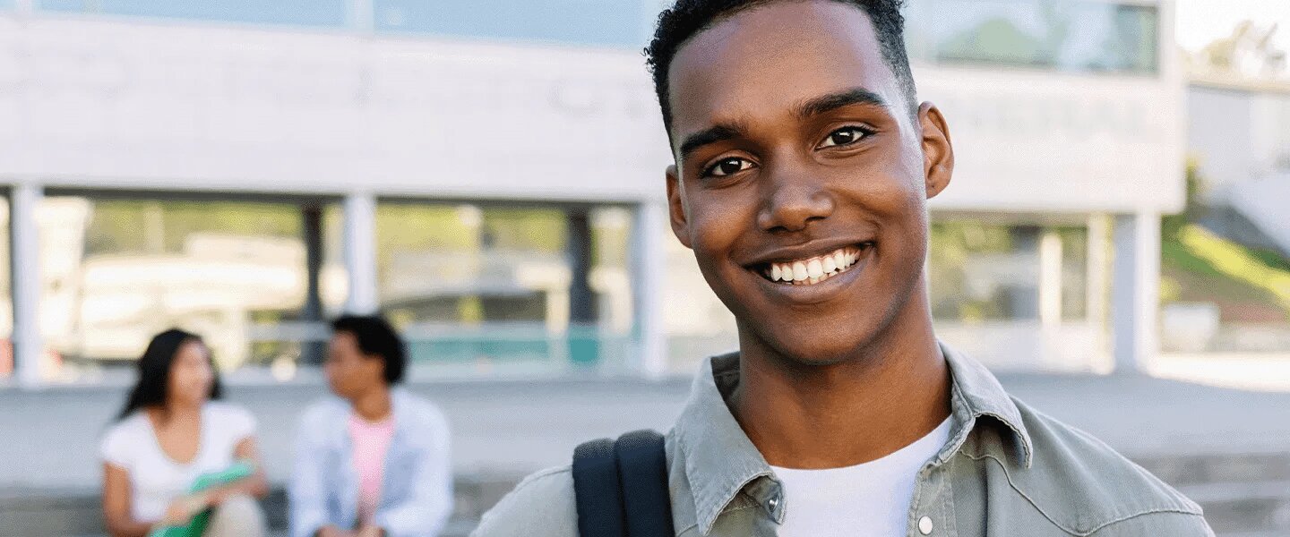 Foto de um estudante negro sorrindo com outros estudantes ao fundo