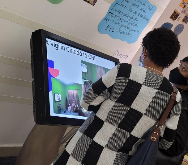 Mulher acessando um terminal eletrônico com a frase "A vigília cidadã ta ON!"