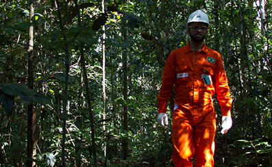 Homem de macacão laranja caminhando com floresta ao fundo