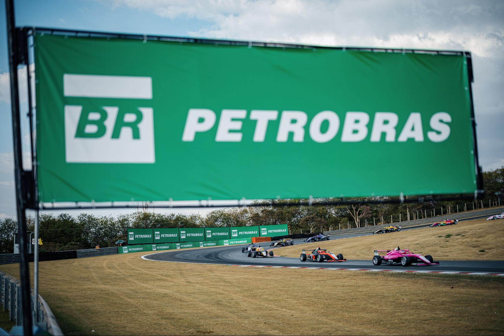 Placa de patrocínio Petrobras em primeiro plano sobre carros de F4.