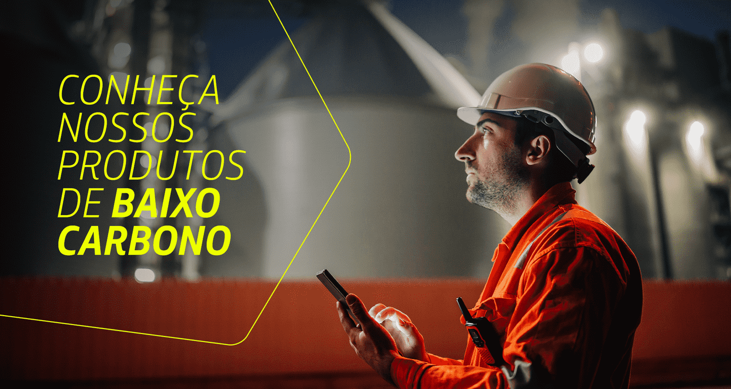 Homem com uniforme da Petrobras olha atentamente para algo fora do campo de visão da imagem. Ele segura um celular. Ao lado dele, está escrito "Conheça nossos produto de baixo carbono"