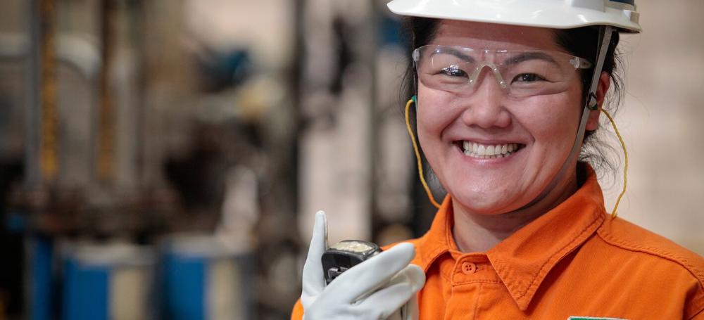 Colaboradora mulher da Petrobras sorrindo para a câmera. Ela está uniformizada utilizando EPIs.