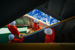 Colaboradores vestidos com macacões laranjas e capacetes brancos, descendo escadas em plataforma