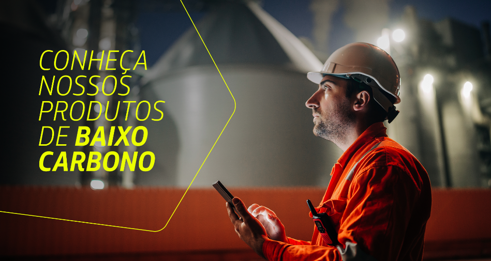 Homem com uniforme da Petrobras olha atentamente para algo fora do campo de visão da imagem. Ele segura um celular. Ao lado dele, está escrito 