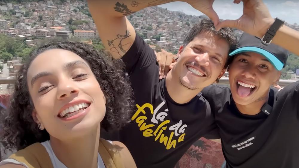 A influenciadora Isabela Reis tirando uma selfie com dois homens que juntos fazem um coração com as mãos.