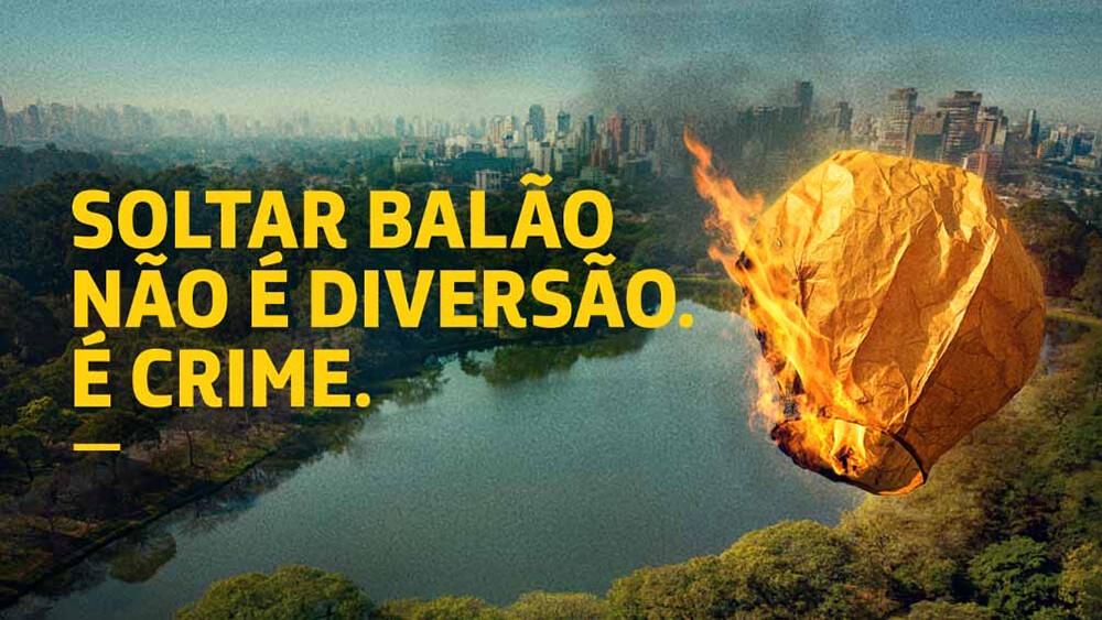 Balão de papel em chamas voando em frente a uma cidade, junto à frase Soltar balão não é diversão, é crime.