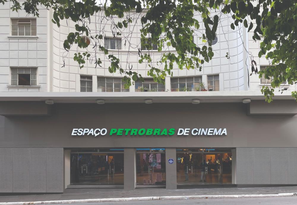A fachada de um cinema chamado ESPAÇO PETROBRAS DE CINEMA com a palavra PETROBRAS em verde. A parte superior do edifício tem janelas e folhagem de árvores.